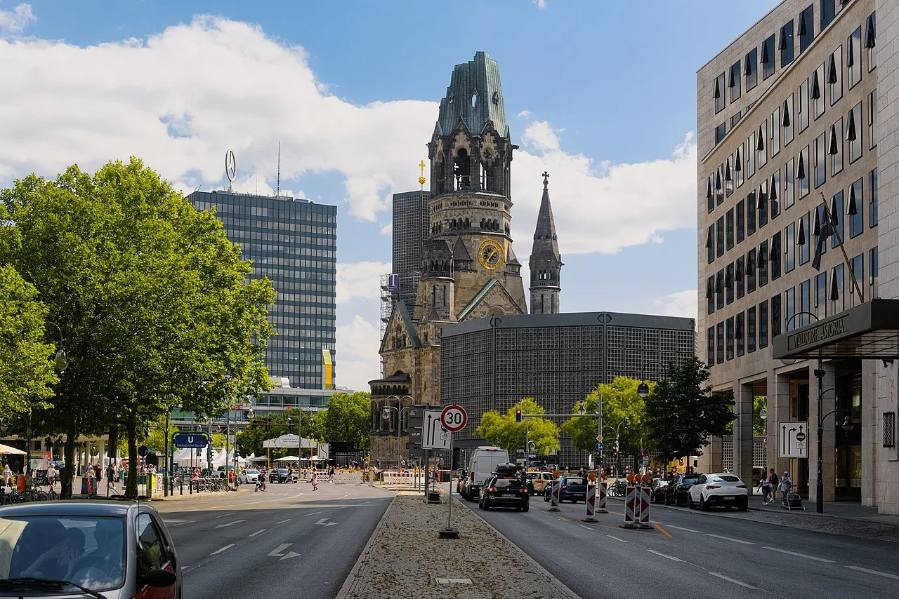 De Kaiser-Wilhelm-Gedächtniskirche in Berlijn bij avond, met de ruïnetoren verlicht naast de blauwe moderne koepelkerk
